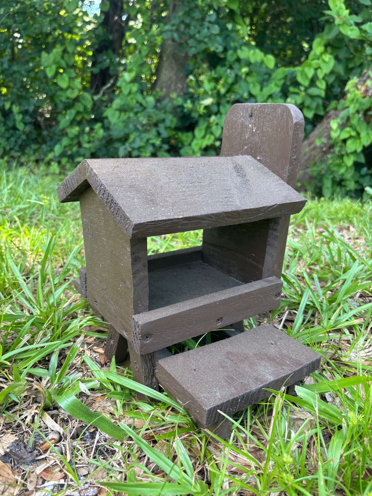 A brown handcrafted bird feeder by Paul Allabaugh, with a peaked roof and feeding tray