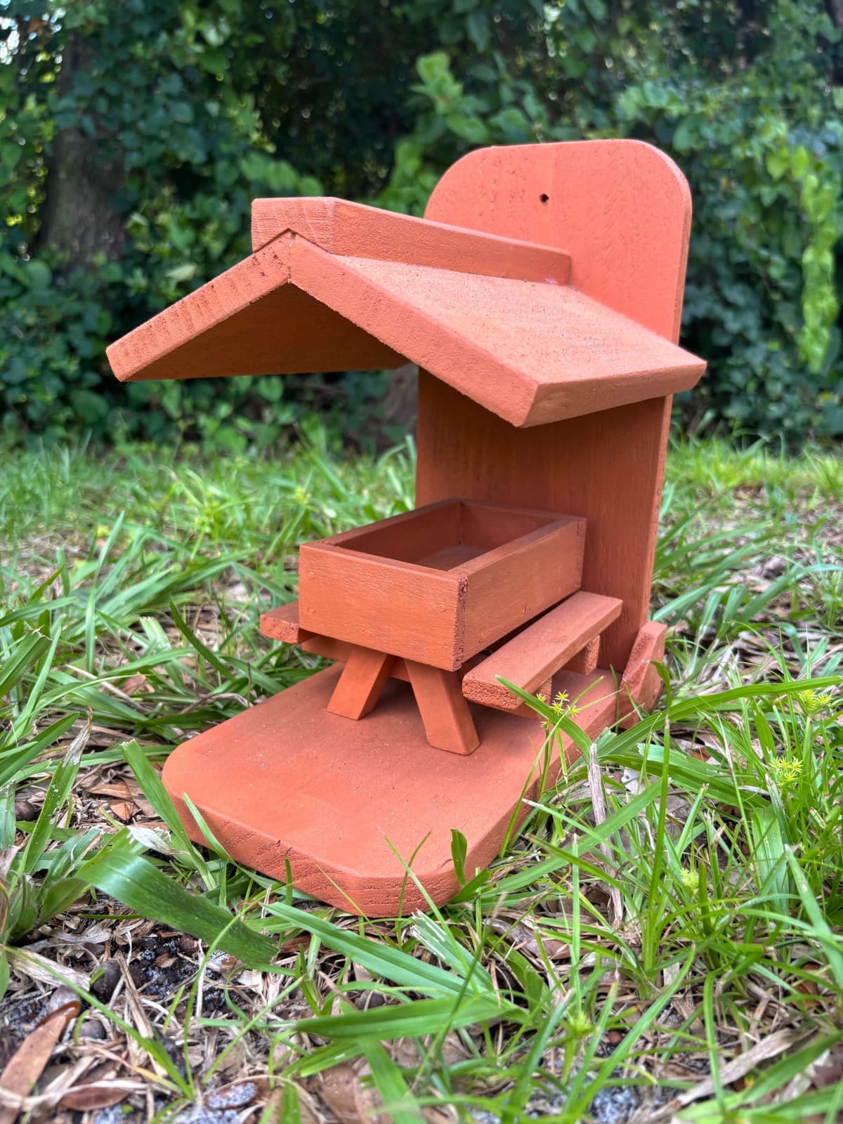 A burnt orange handcrafted bird feeder by Paul Allabaugh, with a peaked roof and feeding tray
