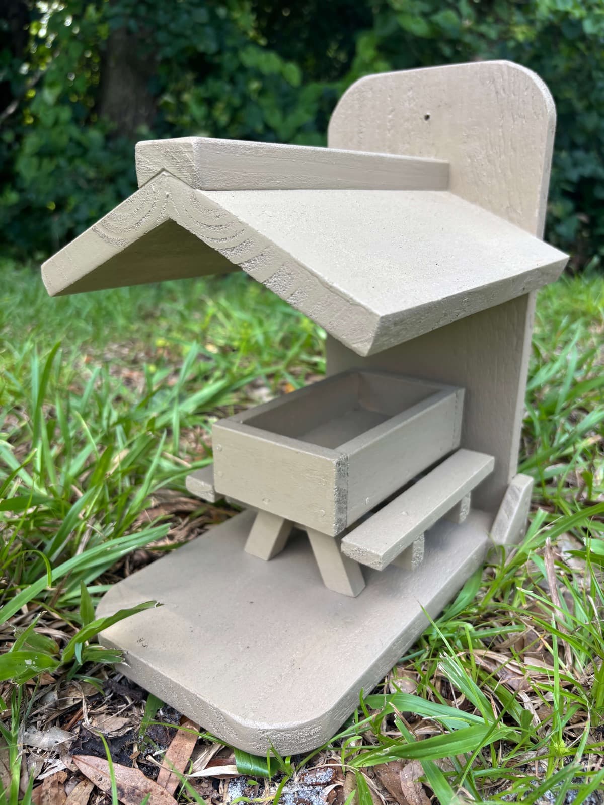 A grey handcrafted bird feeder by Paul Allabaugh, with a peaked roof and feeding tray