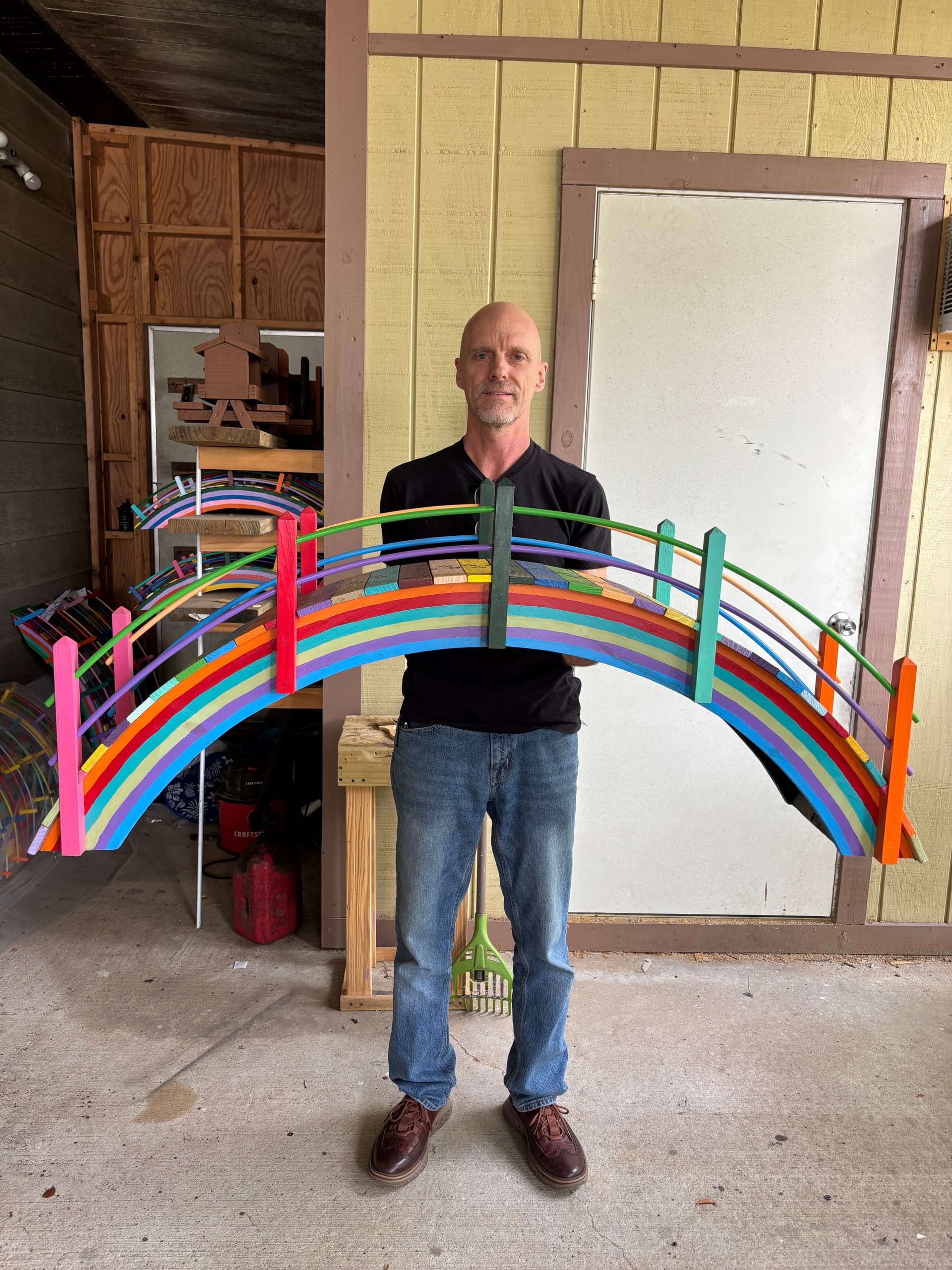 Jason Laird holding Paul Allabaugh's last large rainbow bridge on the porch in front of Paul's workshop in New Smyrna Beach, with more of Paul's bridges visible behind him.