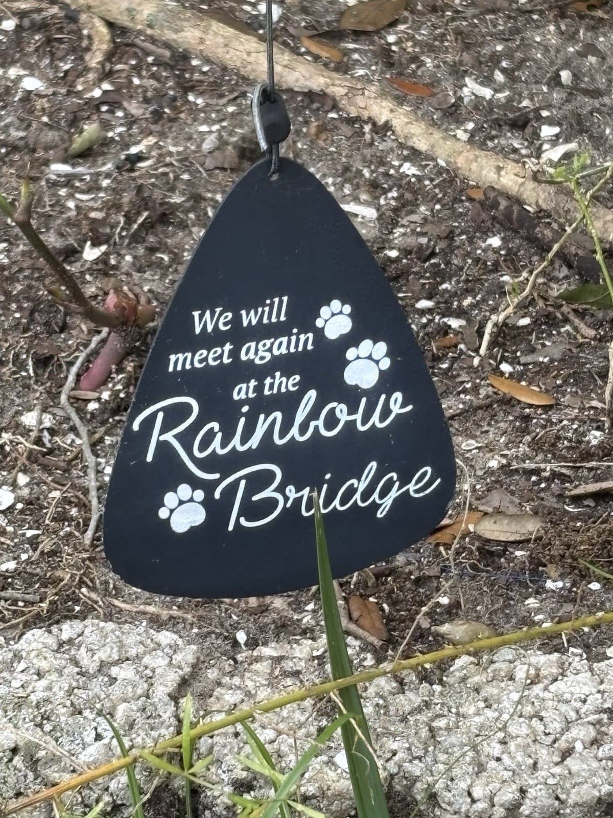 A metal yard ornament that reads 'We Will Meet Again at the Rainbow Bridge', handmade for memorial gardens