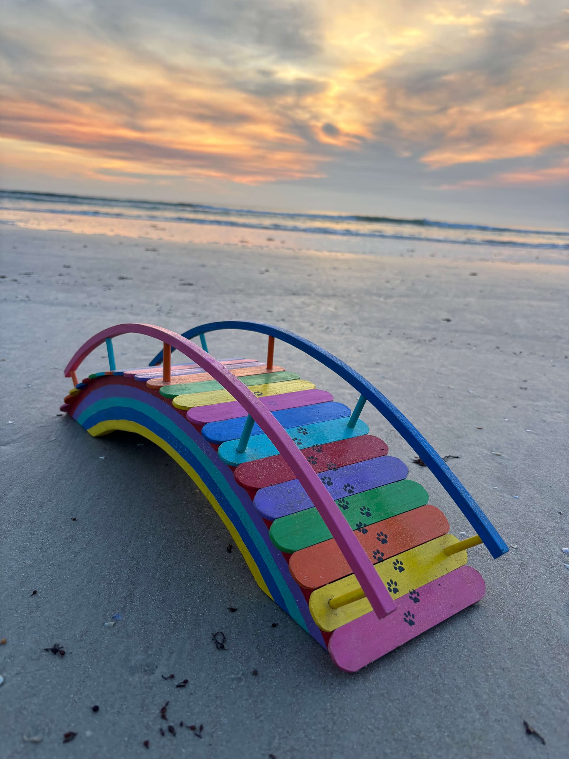 One of Paul Allabaugh's handmade rainbow bridges standing against the sunrise at the edge of the beach
